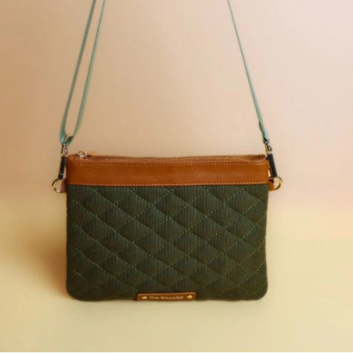 Upright front view of a dark green quilted cotton canvas sling bag with leather trims