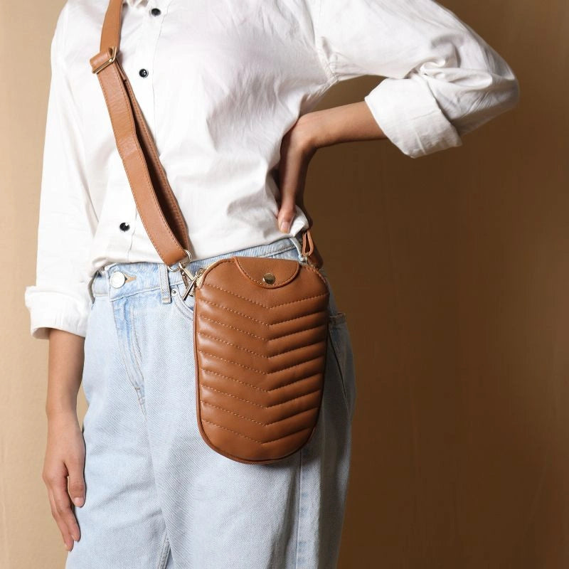 Woman in a white shirt wearing a leather quilted crossbody sling pouch in tan across her body