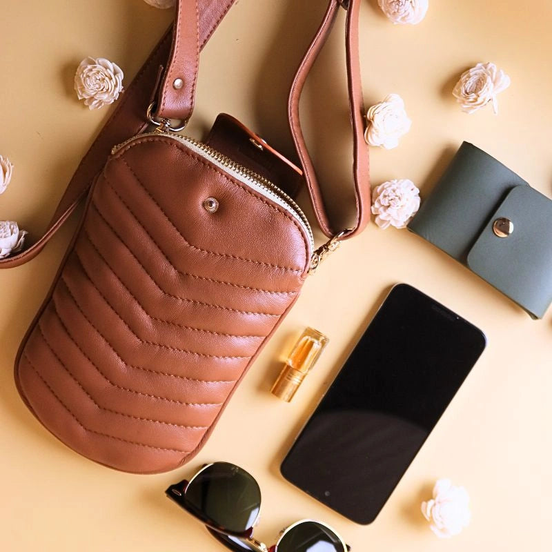 Top View of a Tan Quilted Leather Shoulder crossbody sling pouch bag with a cellphone, a green card case, and white flowers strewn around next to it