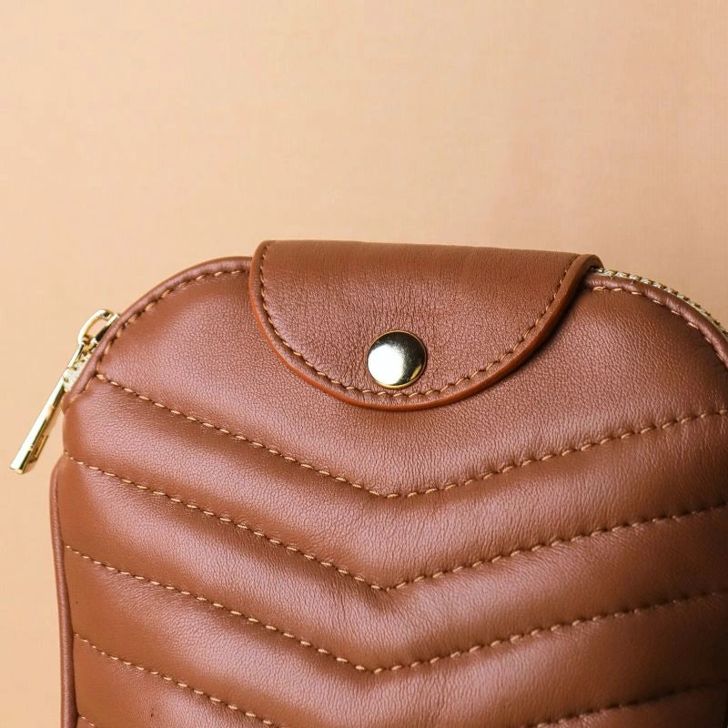 Stitching detail and a golden button of a tan quilted leather pouch bag with a golden zip