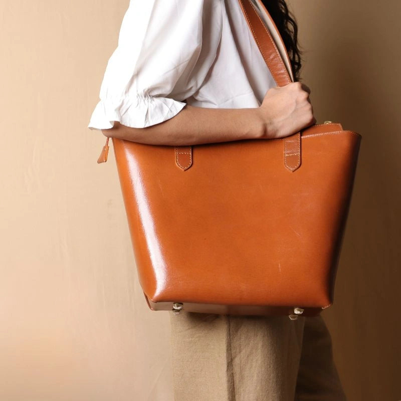 Front View of a Tan Leather Tote Bag with a zipped closure carried by a woman with a white shirt