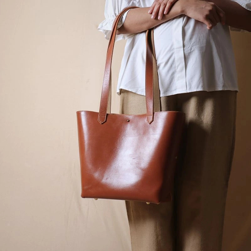 Woman holding a tan leather tote handbag in her arms