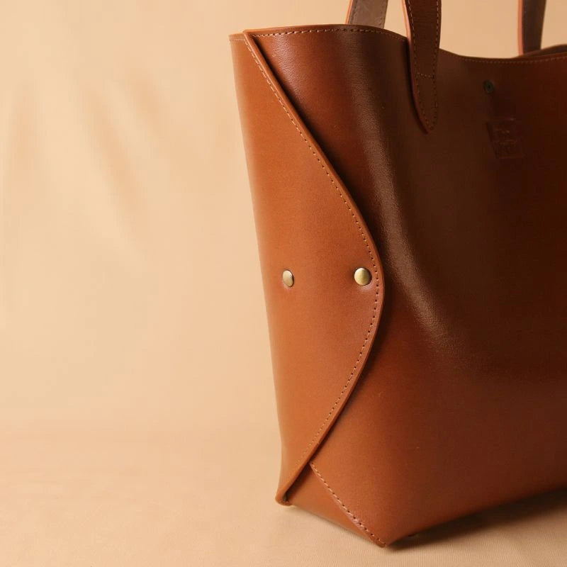 Detailed side view of two brushed gold rivets of a leather tote bag in tan