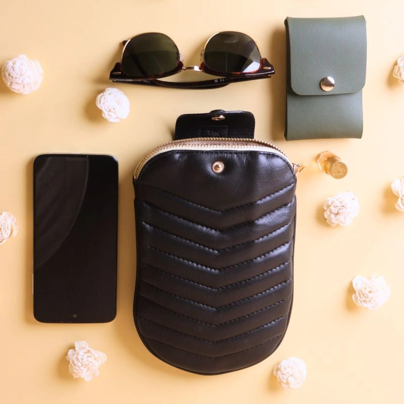top view of a small black quilted leather pouch bag with a cell phone, pair of sunglasses and a olive green card case next to it