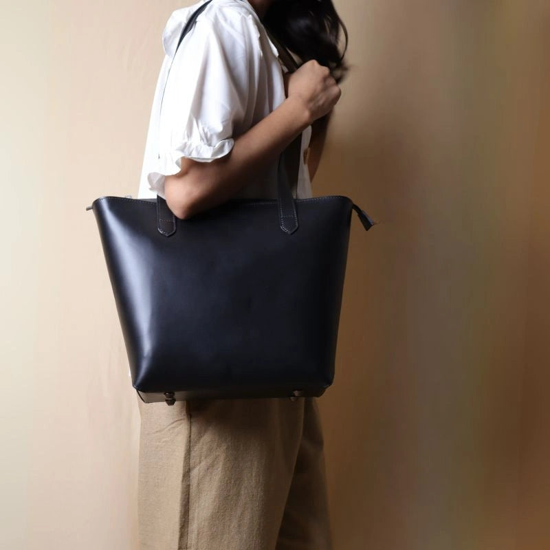 Black Leather Horizontal Tote Bag with zipped closure carried by a woman over her shoulder in a white shirt.