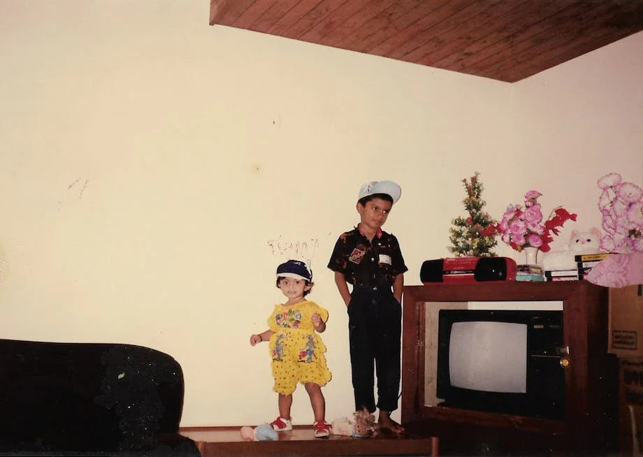 A 90's family image of a brother and a sister standing next to each other in their family home  